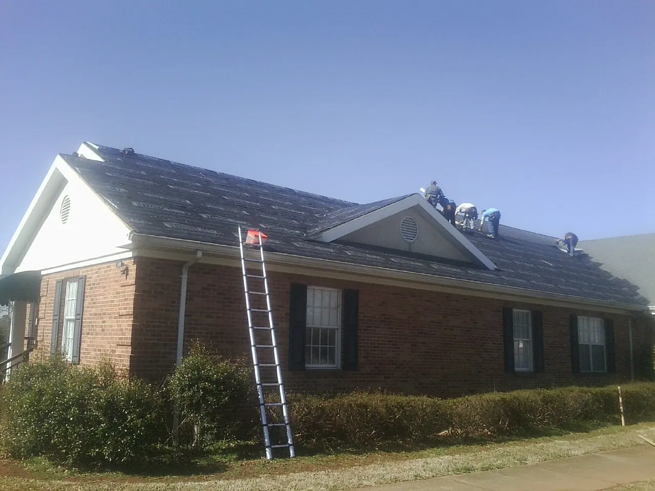 Crew tearing shingles off a brick ranch roof with a ladder set — Emergency Roof Repair work by our crew in Franconia