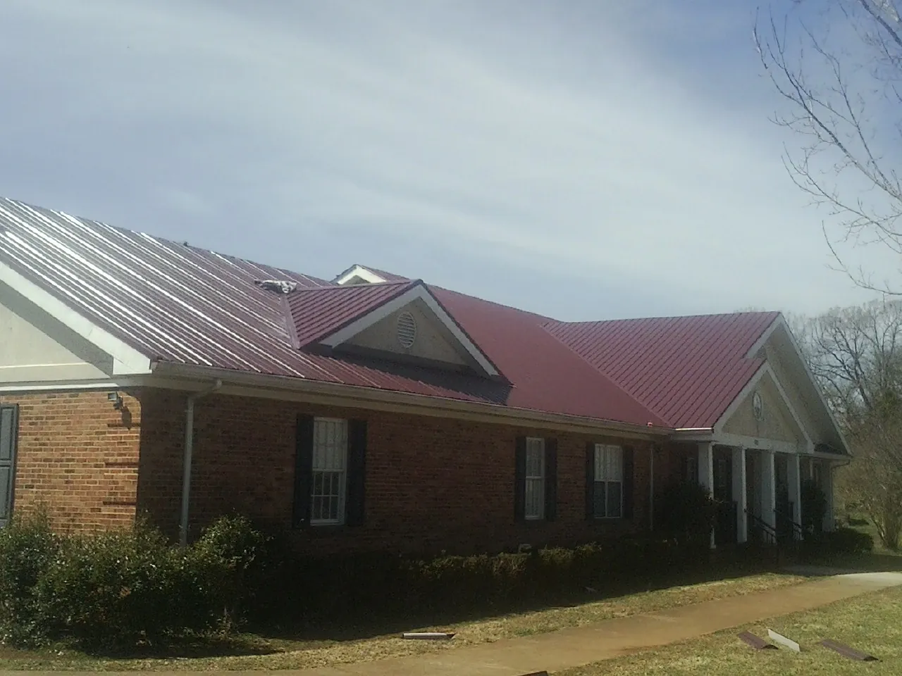 Red metal roof with gabled entries on a long brick building, from a Hail Damage Roof Repair job in Franconia
