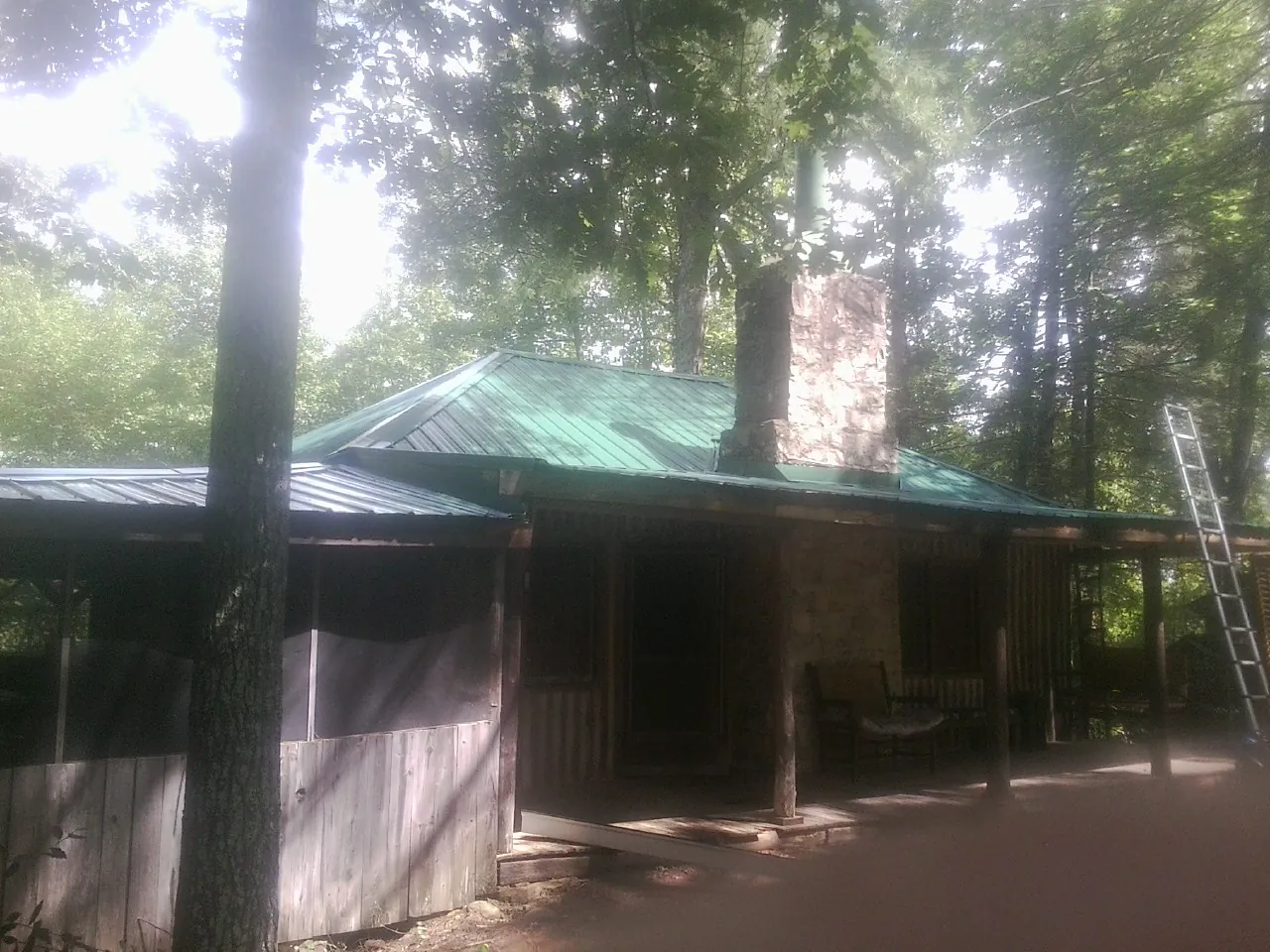 Green metal roof and stone chimney above a log cabin porch in Franconia