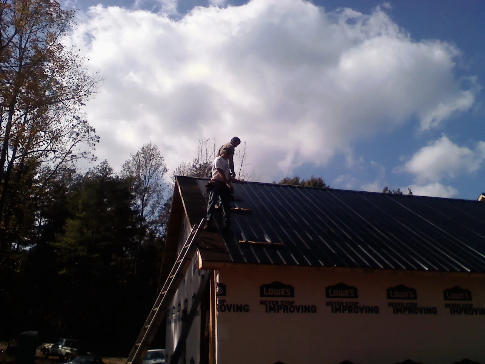 Roofer fastening dark metal panels high against a cloudy sky, from a Roof Inspection job in Franconia