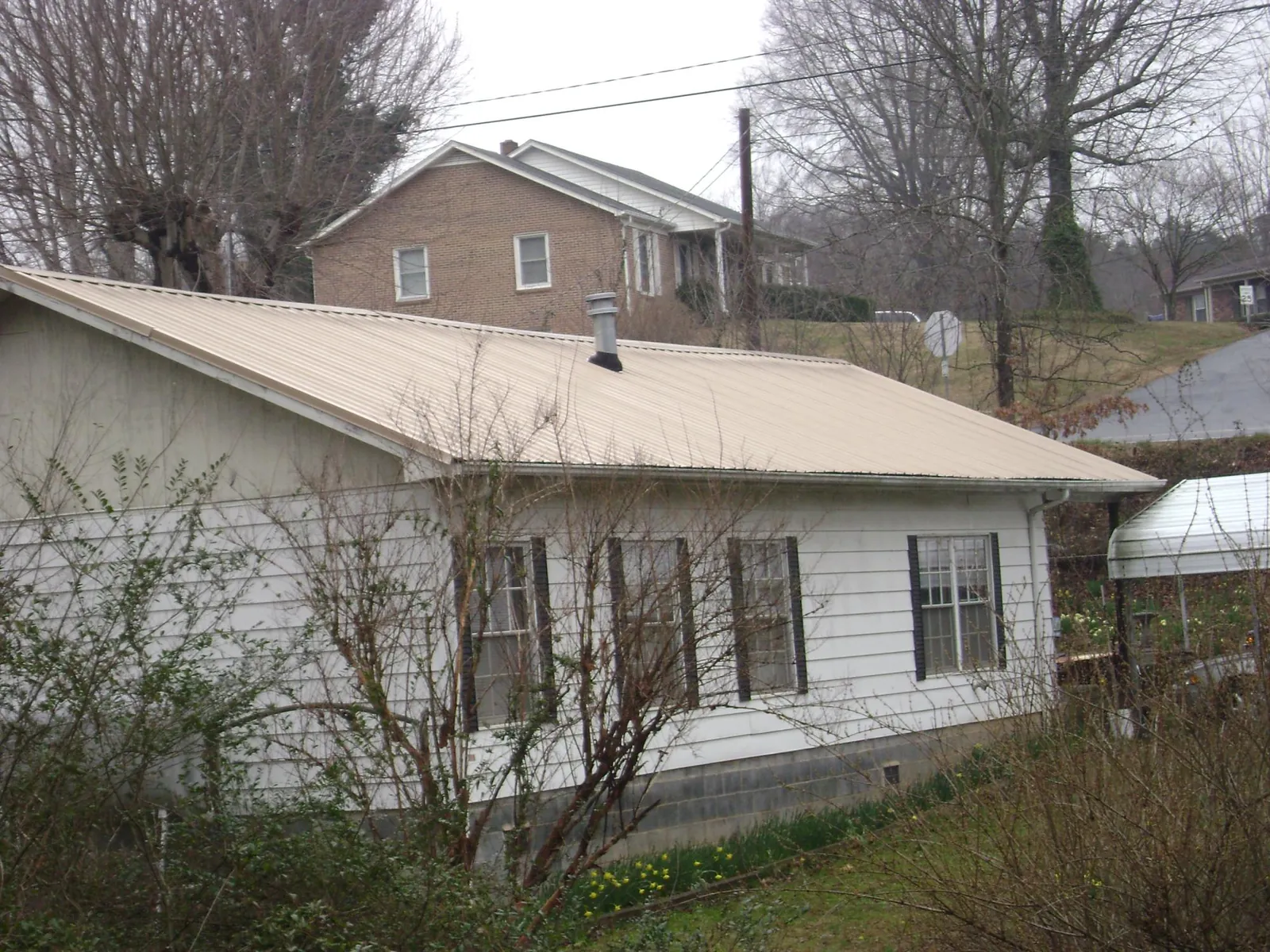 Tan metal roof on a white sided house set into a hillside — Commercial Roofing by Roofing Brothers in Franconia